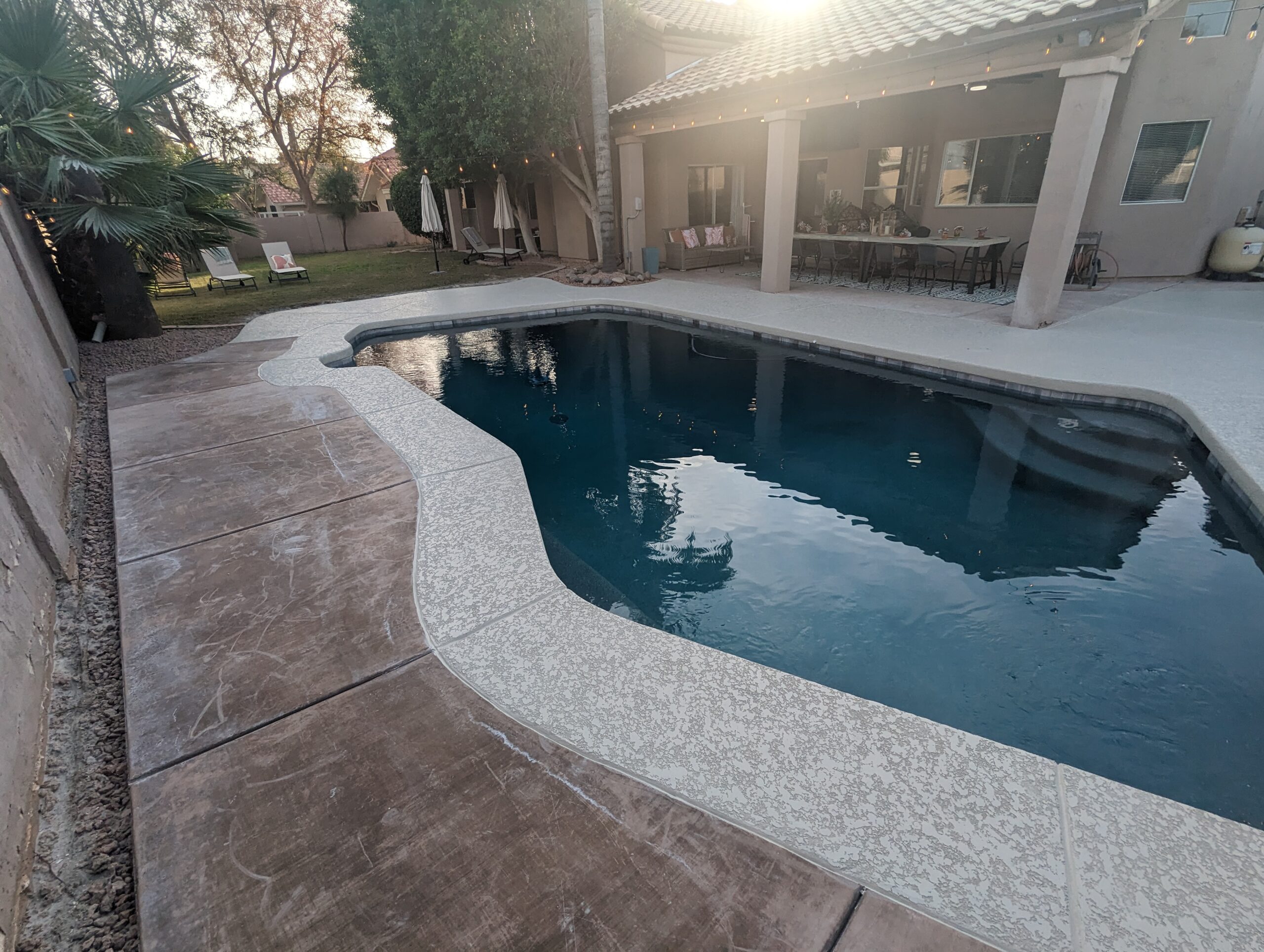 Backyard pool with clean water, surrounding concrete deck, and lounge chairs, showcasing a well-maintained residential pool area by Pelican Pools in Gilbert, AZ.