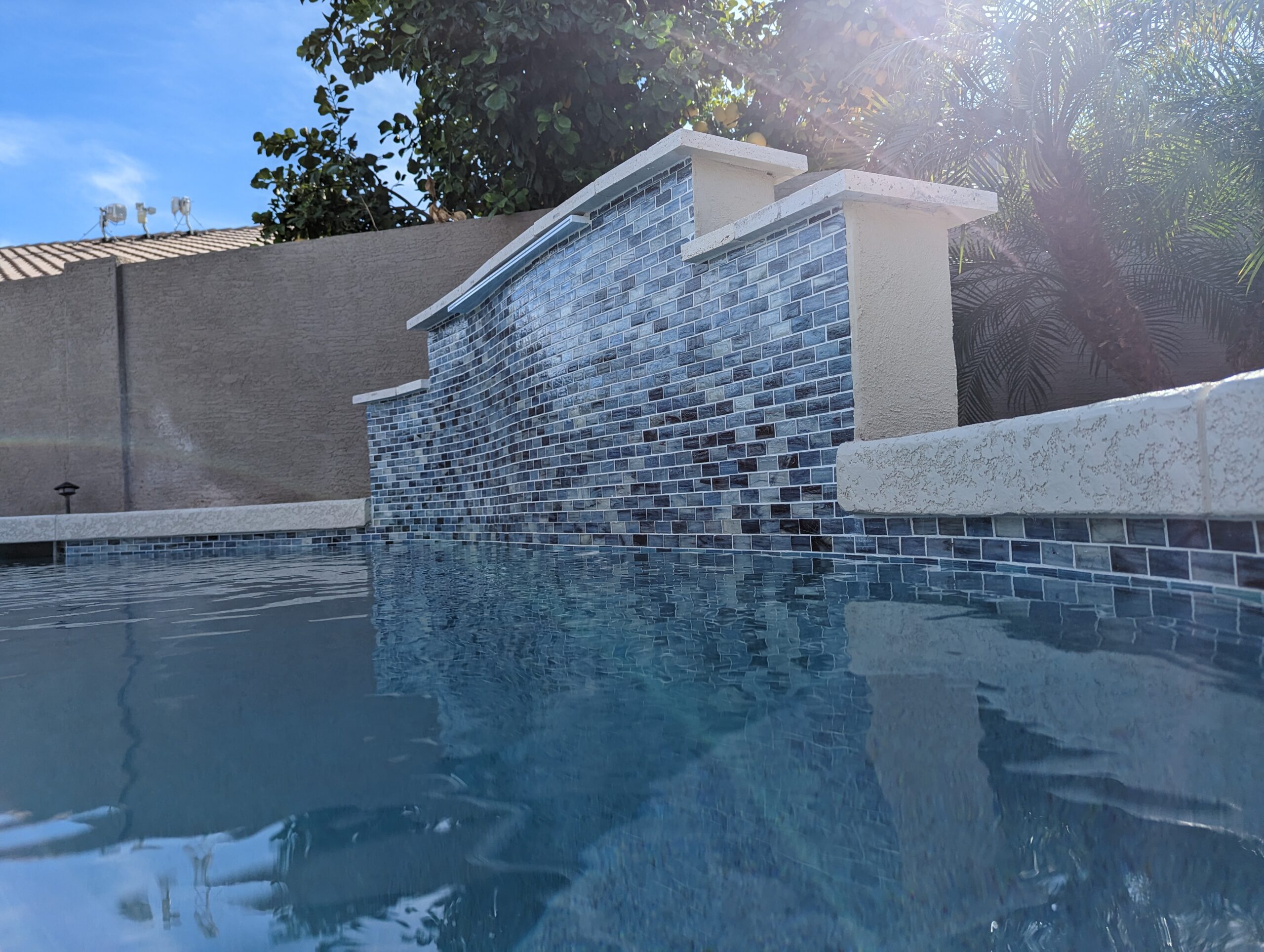 Pool with modern tile design and water features, surrounded by lush greenery, showcasing high-quality pool aesthetics and maintenance by Pelican Pools.