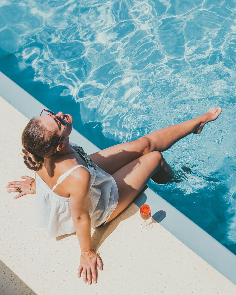 Woman relaxing by a sparkling pool, enjoying a drink, embodying the leisure and enjoyment associated with professional pool service and maintenance from Pelican Pools in Gilbert, AZ.