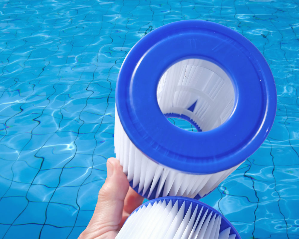 Pool filter cartridge held above clear blue water, highlighting pool maintenance and equipment replacement services by Pelican Pools.