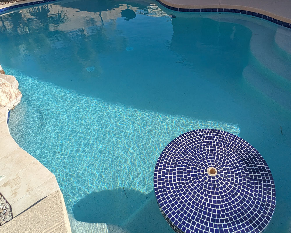 Pool with crystal-clear water and a blue mosaic fountain feature, showcasing a modern and inviting design, emphasizing pool remodels and upgrades.