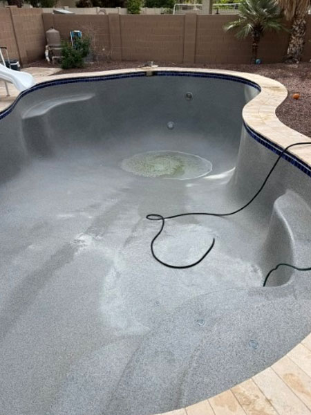 Empty pool undergoing remodeling, showcasing gray resurfacing with visible plumbing connections, highlighting Pelican Pools' upgrade services for improved efficiency and aesthetics.