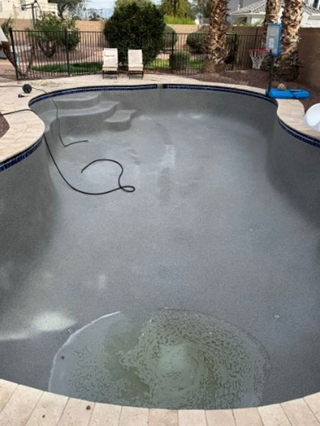 Empty pool with gray surface and visible water swirl, surrounded by landscaped area, showcasing potential for remodeling and upgrades by Pelican Pools.