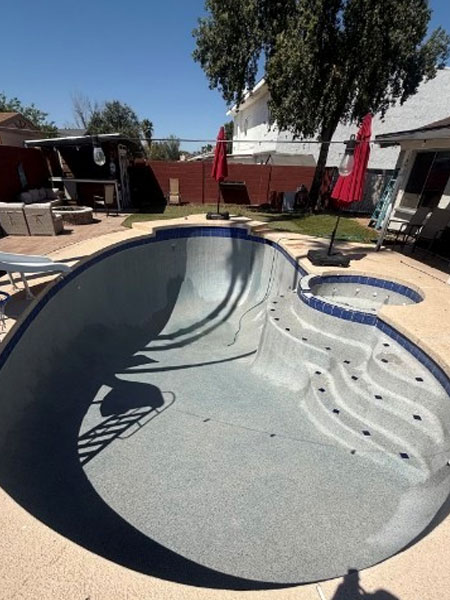 Empty swimming pool with steps, surrounded by patio furniture and umbrellas, showcasing the need for professional cleaning and restoration services.